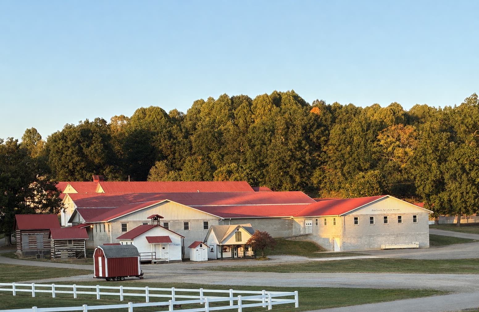 Exterior view of the Knox County Agricultural Museum, its red-roofed buildings framed by trees and a white fence at golden hour.